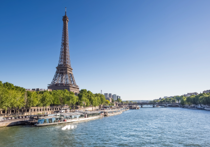 Eiffelturm an der Seine, mit grünen Ufern, klarem Himmel und vorbeifahrenden Booten