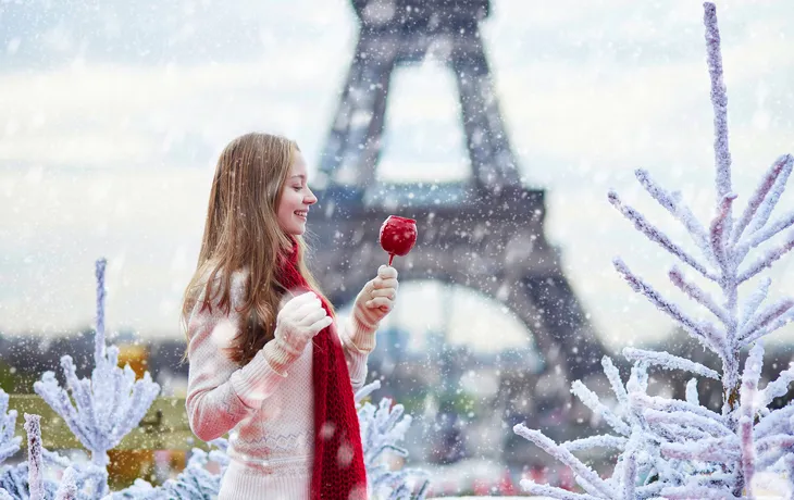 Frau im Schnee mit Lutscher vor Eiffelturm in Paris.
