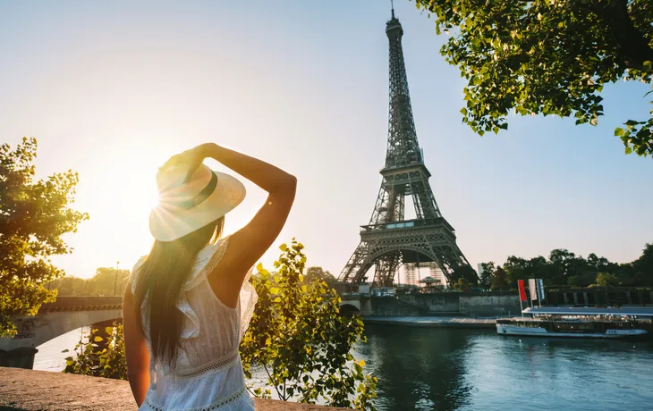 Frau mit Hut betrachtet den Eiffelturm bei Sonnenuntergang.