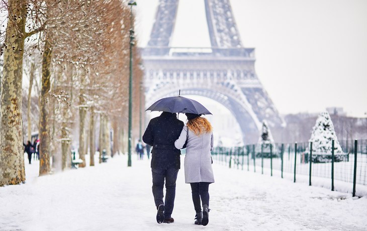 Paar unter Regenschirm im Schnee vor dem Eiffelturm in Paris.