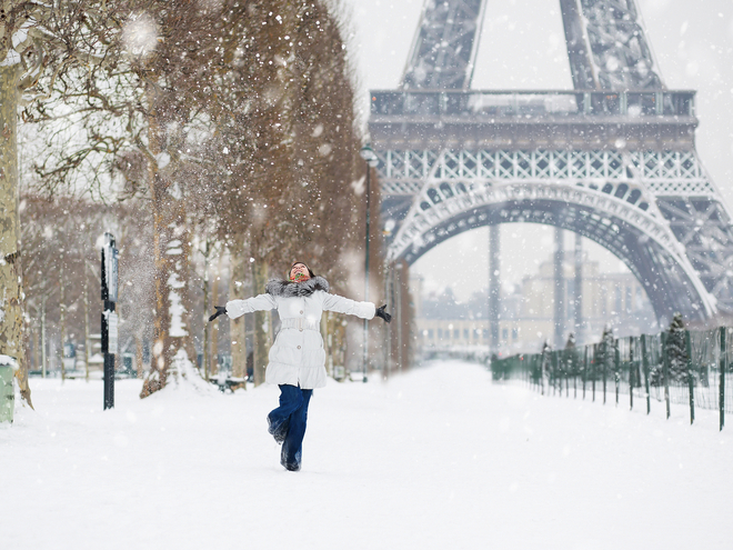 Eine Person steht mit ausgebreiteten Armen im Schnee vor dem Eiffelturm in Paris im Winter.